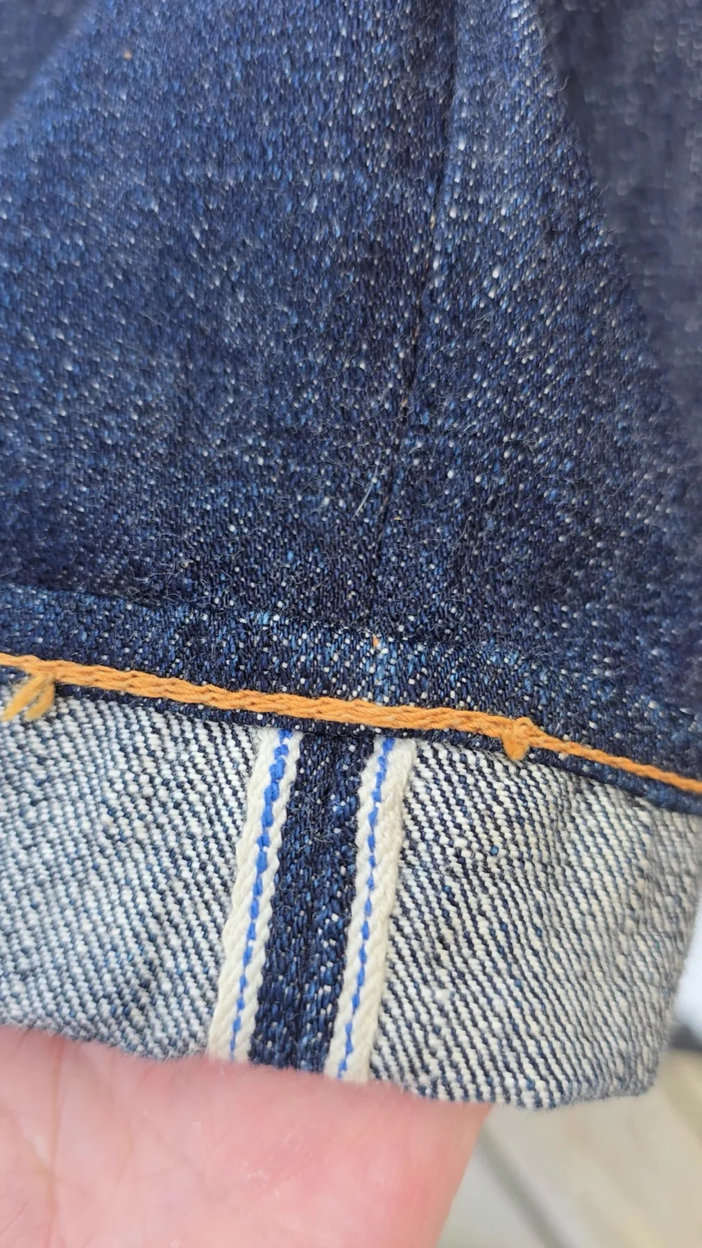 Macro shot of folded raw denim showing a blue selvedge thread along the fabric edge.