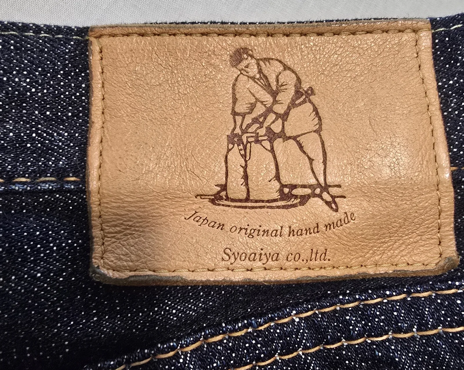 A deerskin leather patch on the back of a pair of indigo jeans that depicts a man dyeing indigo.