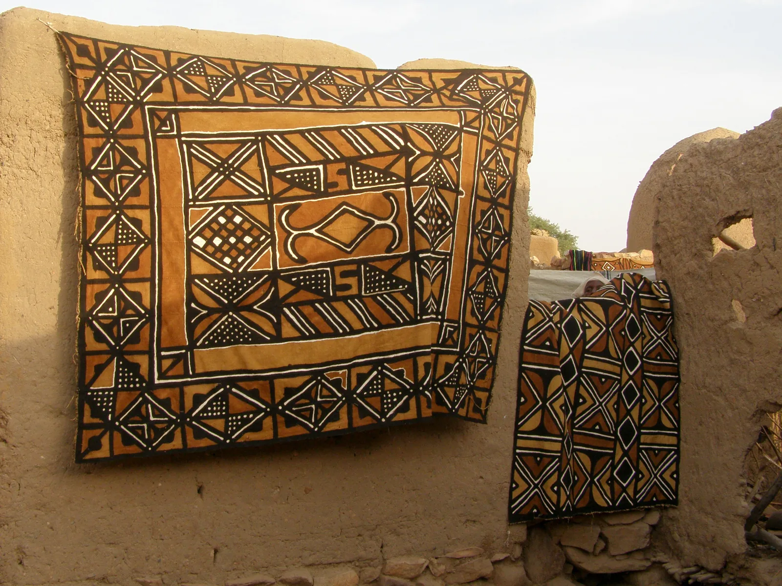 Patterned brown and cream bogolan mud cloth hanging to dry against a mud-brick wall in Mali