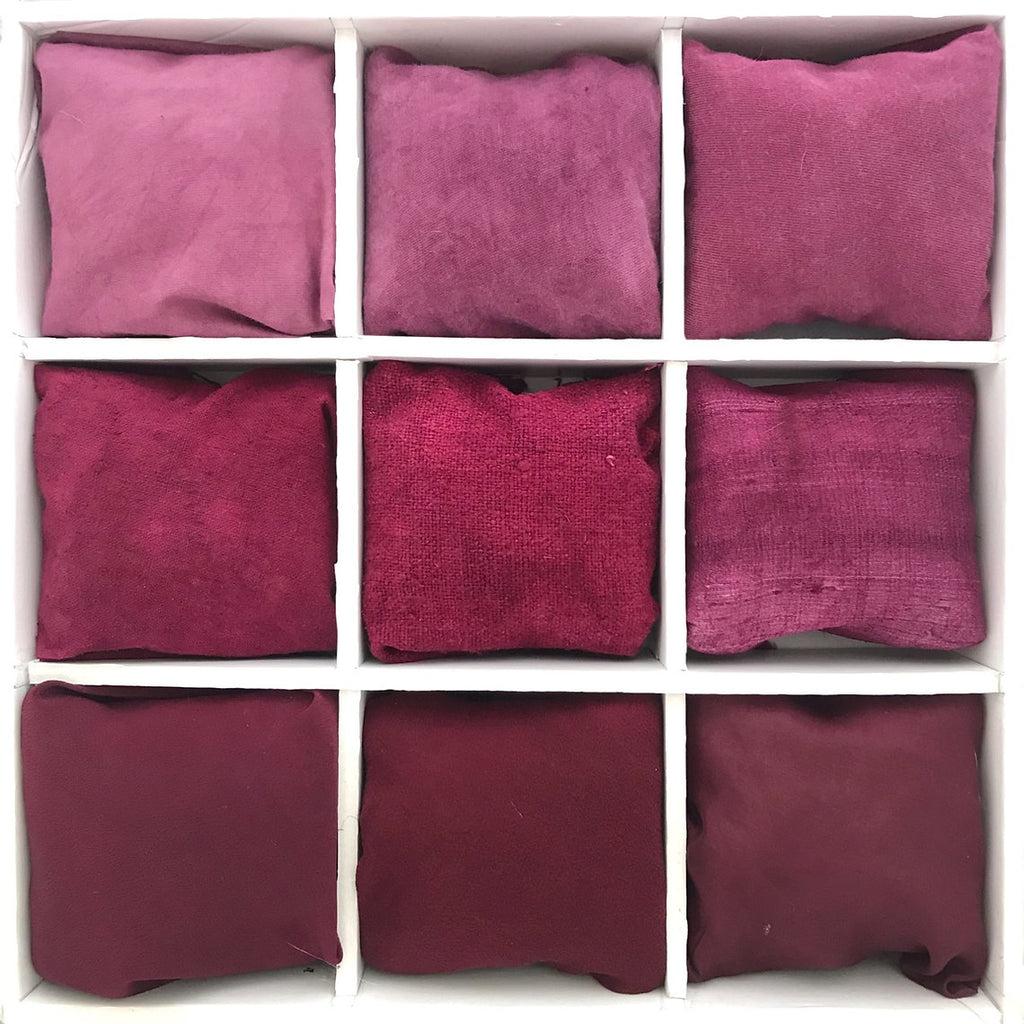 Nine swatches of lac-dyed fiber, each modified with a different mordant