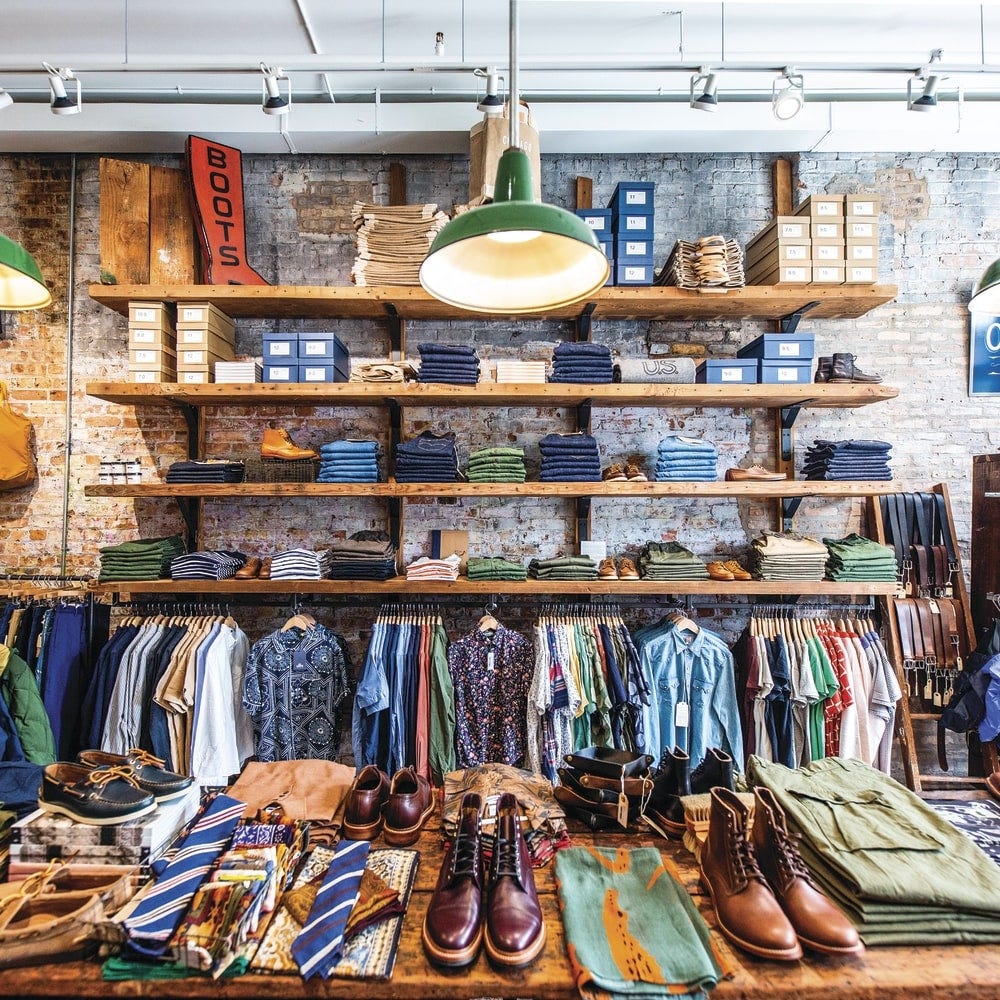 Interior of Independence menswear shop in Chicago, with wood shelving of folded denim and shoeboxes against an exposed brick wall, and a vintage Boots sign above.