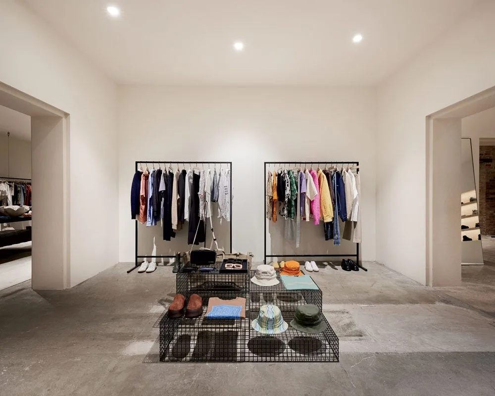 Minimalist white-walled interior of Notre in Chicago's West Loop, with two freestanding clothing racks and wire display tables holding shoes, hats, and accessories on a polished concrete floor.