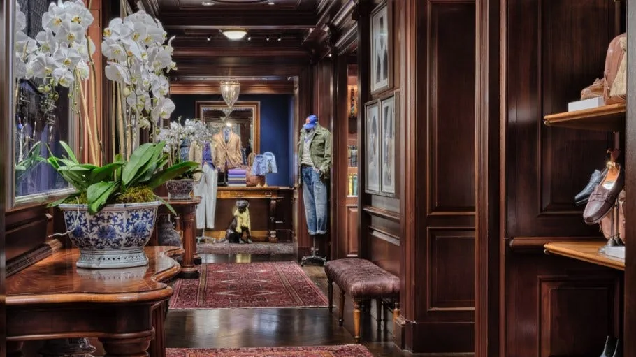 Dark wood-paneled interior of the Ralph Lauren Chicago flagship, with fresh orchids in a blue-and-white planter, a Persian rug, and a mannequin dressed in layered menswear in the background.