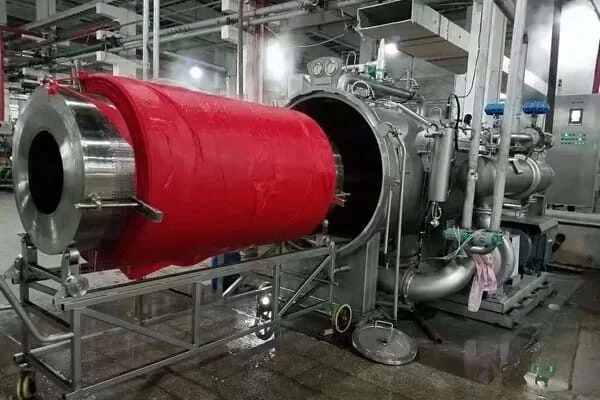 Large cylindrical textile-processing machine with a red fabric roll or drum inside a factory.