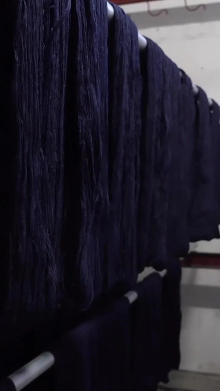 Skeins or hanks of dark indigo yarn hanging vertically during a dyeing process, with saturated blue color visible across the strands.