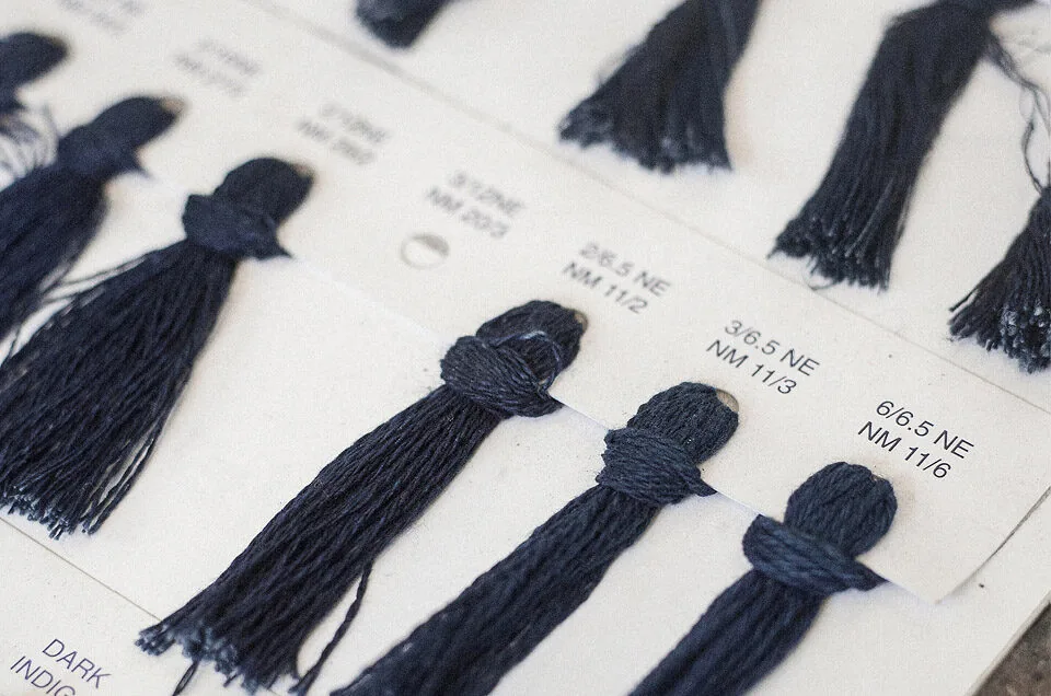 Textile swatches and small bundles of rope-dyed dark blue yarn arranged on a sample board with labels.