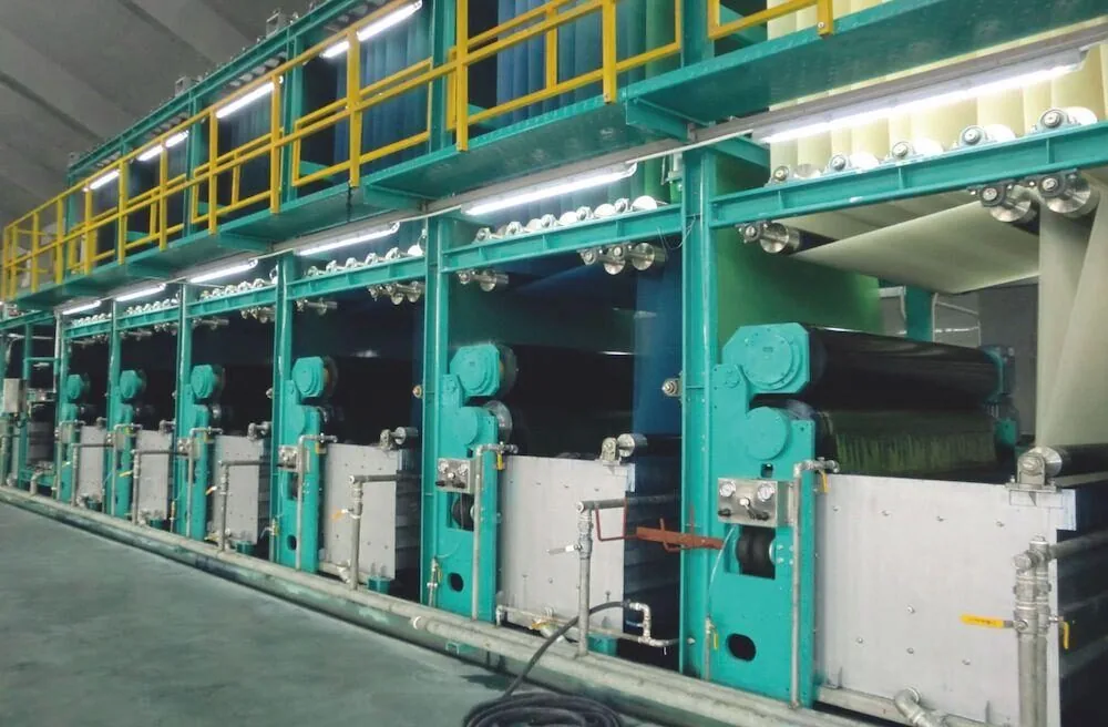 Long industrial textile production line with multiple green and white machines inside a factory.