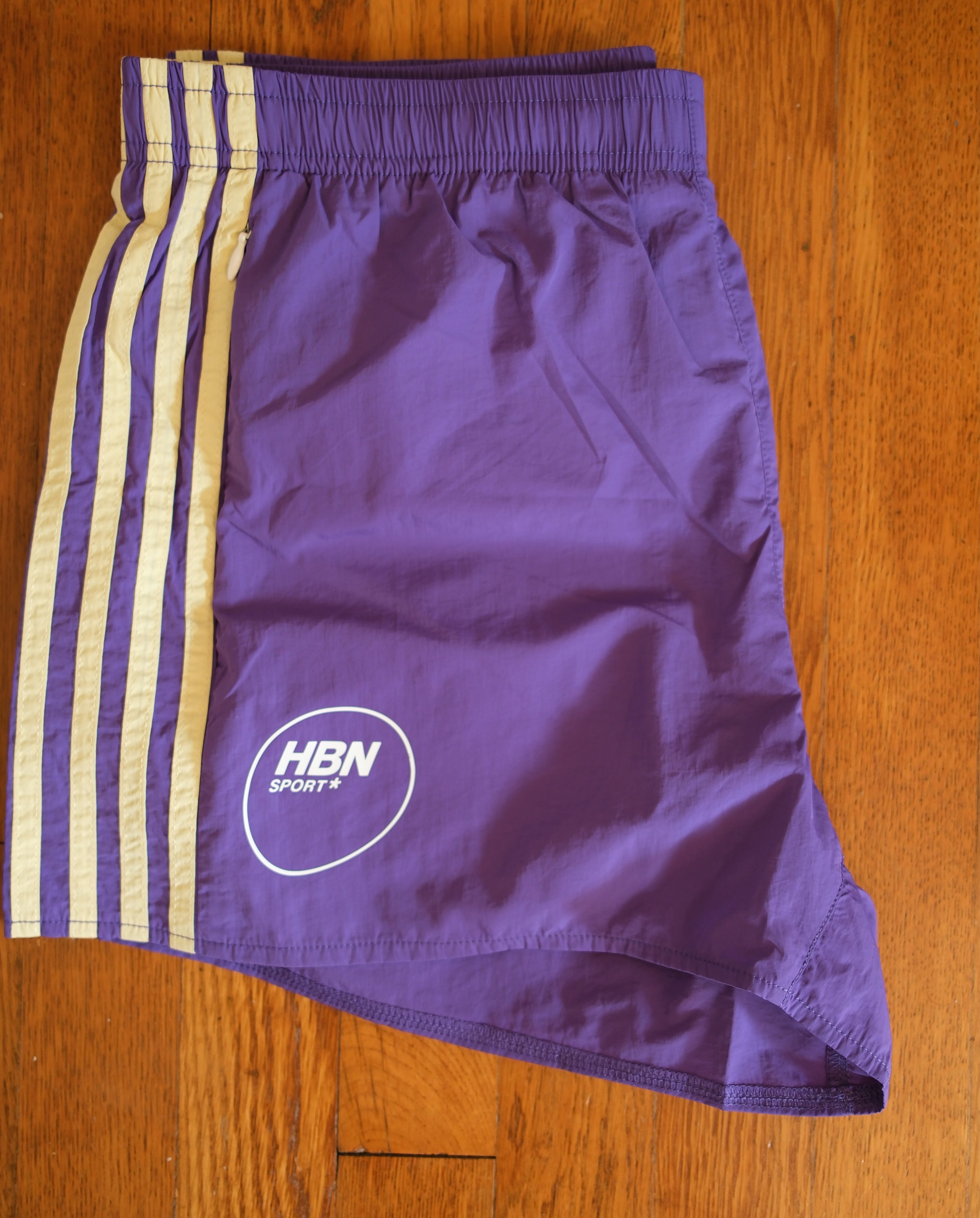 Close-up of the yellow side-stripe lettering and HBN Sport mark on the Human By Nature Seaside Nylon Track Shorts.
