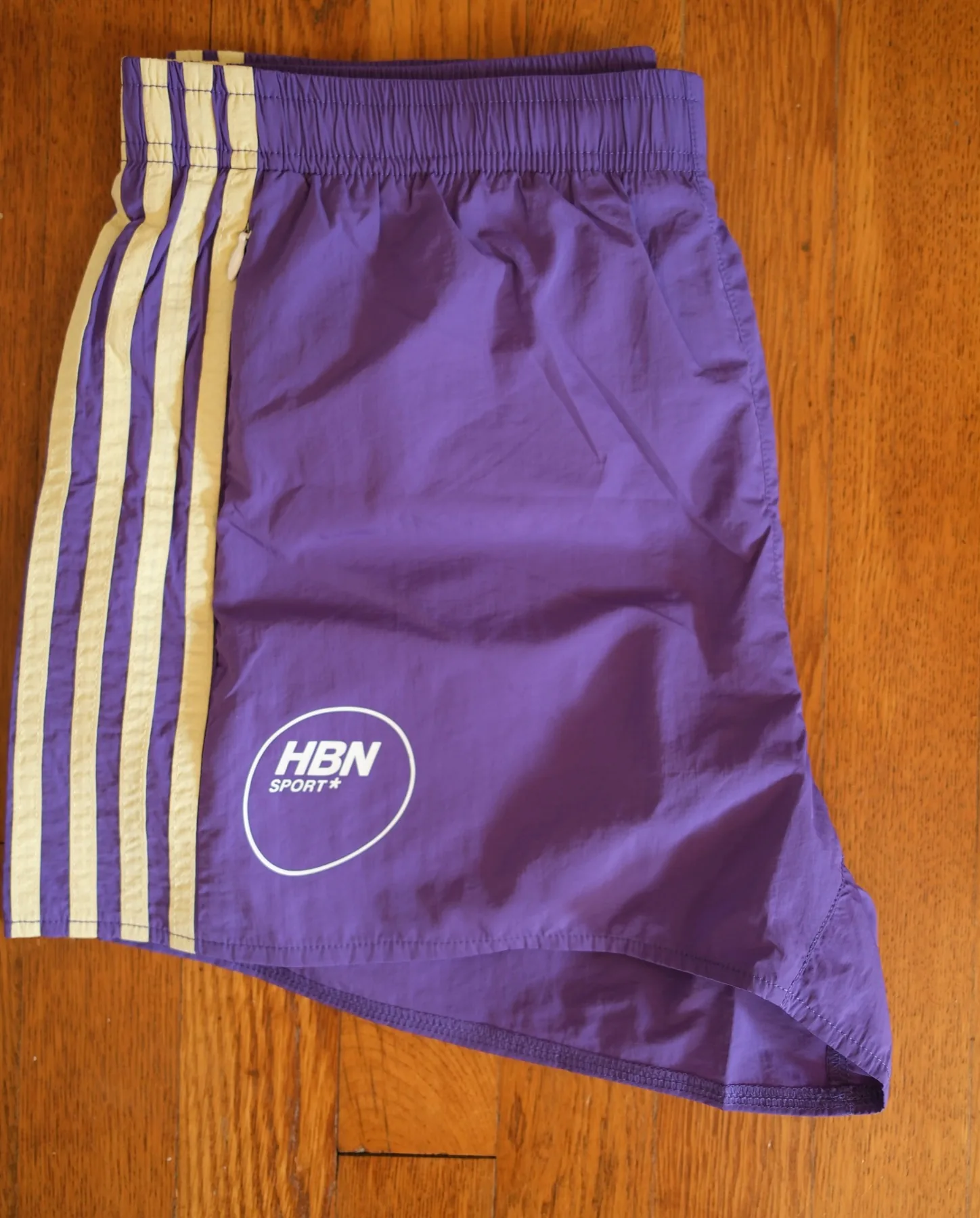 Close-up of the yellow side-stripe lettering and HBN Sport mark on the Human By Nature Seaside Nylon Track Shorts.