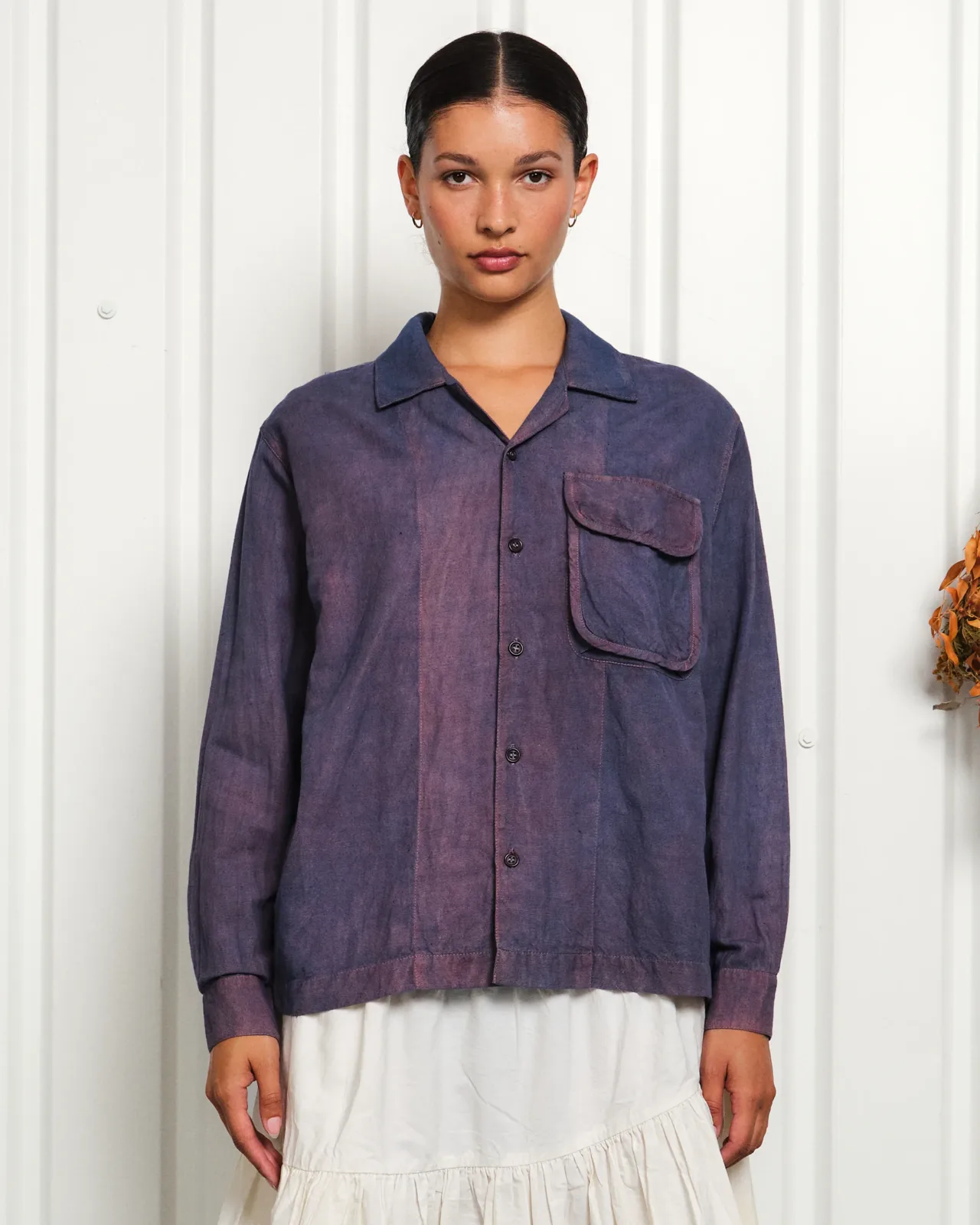 Studio product photo of a model wearing the Story mfg. Greenhouse Shirt, hand-dyed in a mottled indigo and madder purple, against a corrugated white backdrop.